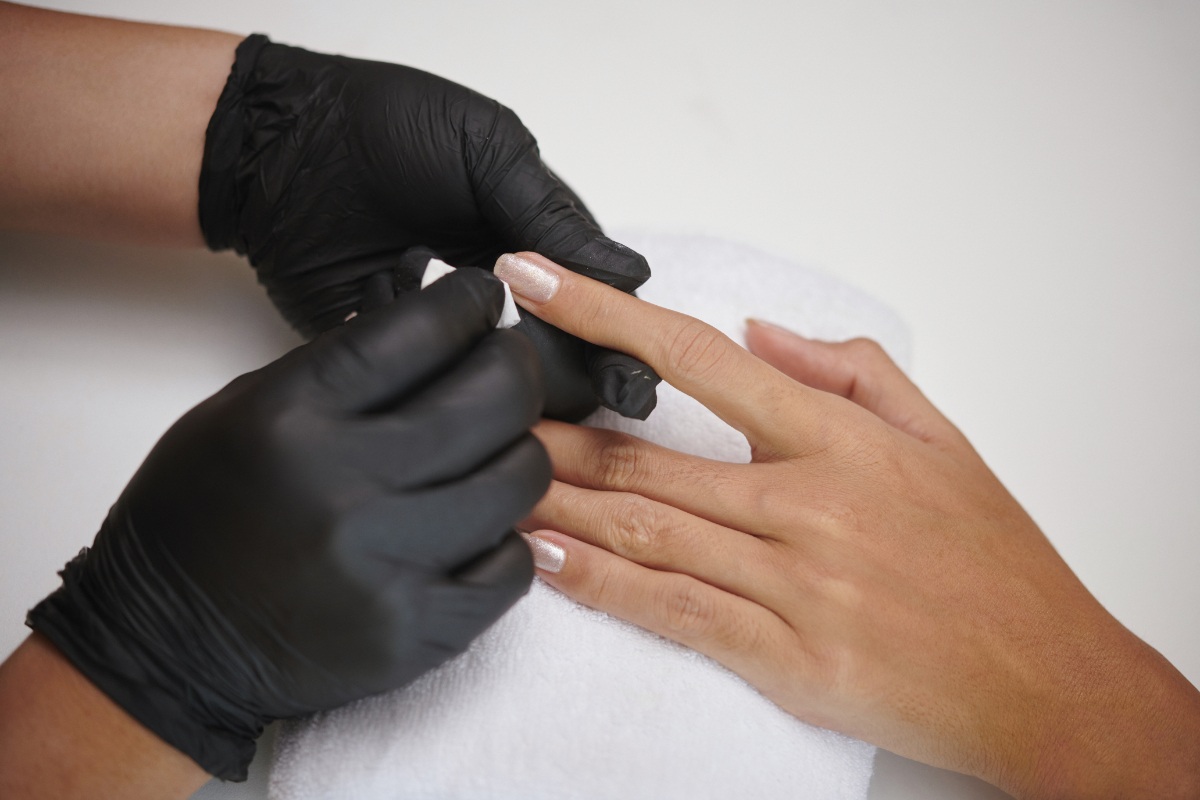 Nail technician in black gloves preparing a client&rsquo;s nails for a traditional manicure